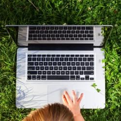 Une personne utilise un ordinateur portable dans l’herbe.