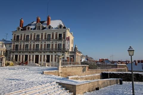 Photo de la façade de la Maison de la magie depuis la place du Château, sous la neige avec un ciel entièrement bleu.