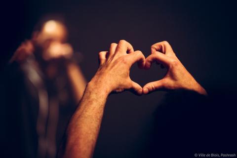 Une personne assistant à un concert forme un cœur avec ses doigts.