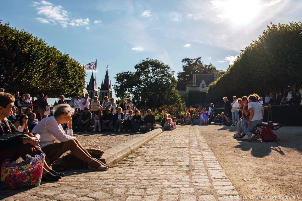Sur la place du Château, le public assiste au spectacle « Place assise », par le collectif Bim.