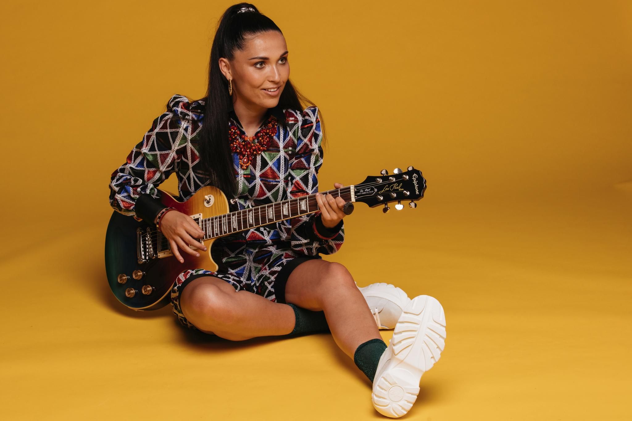 Camille Esteban, souriante, jouant de la guitare par terre.